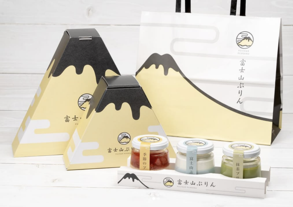 富士山布丁的精美包裝,包括富士山造型的禮盒和手提袋,內含多種口味布丁,如抹茶、彈珠汽水和季節限定水果口味,完美呈現富士山的自然風貌與優雅設計